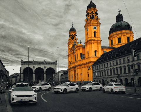 Bright yellow baroque church towers dominate a city street with Uber cars parked along the curb, gray surrounding buildings behind them.