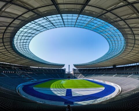 Panoramic view of an empty modern stadium with a circular glass roof opening and a green field.