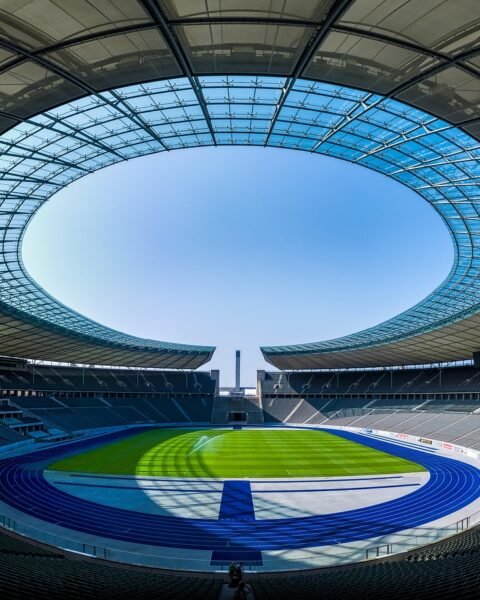 Panoramic view of an empty modern stadium with a circular glass roof opening and a green field.