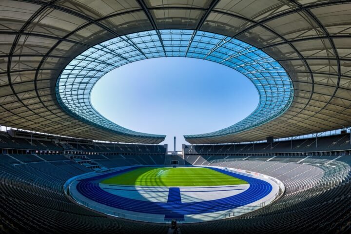 Panoramic view of an empty modern stadium with a circular glass roof opening and a green field.