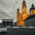 Bright yellow baroque church towers dominate a city street with Uber cars parked along the curb, gray surrounding buildings behind them.