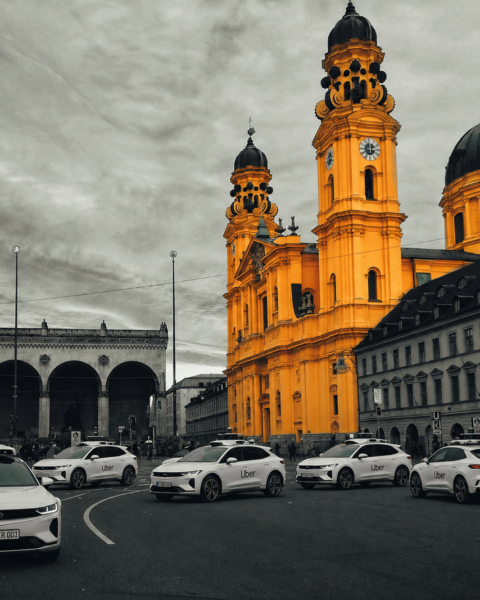 Bright yellow baroque church towers dominate a city street with Uber cars parked along the curb, gray surrounding buildings behind them.