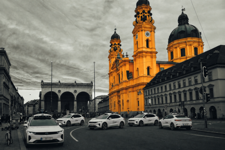 Bright yellow baroque church towers dominate a city street with Uber cars parked along the curb, gray surrounding buildings behind them.